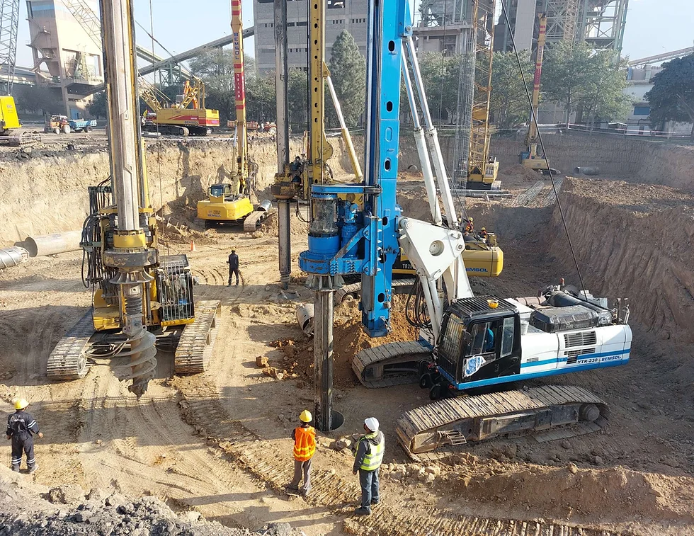 Two large rotary piling rigs working in a deep industrial excavation with tower cranes overhead